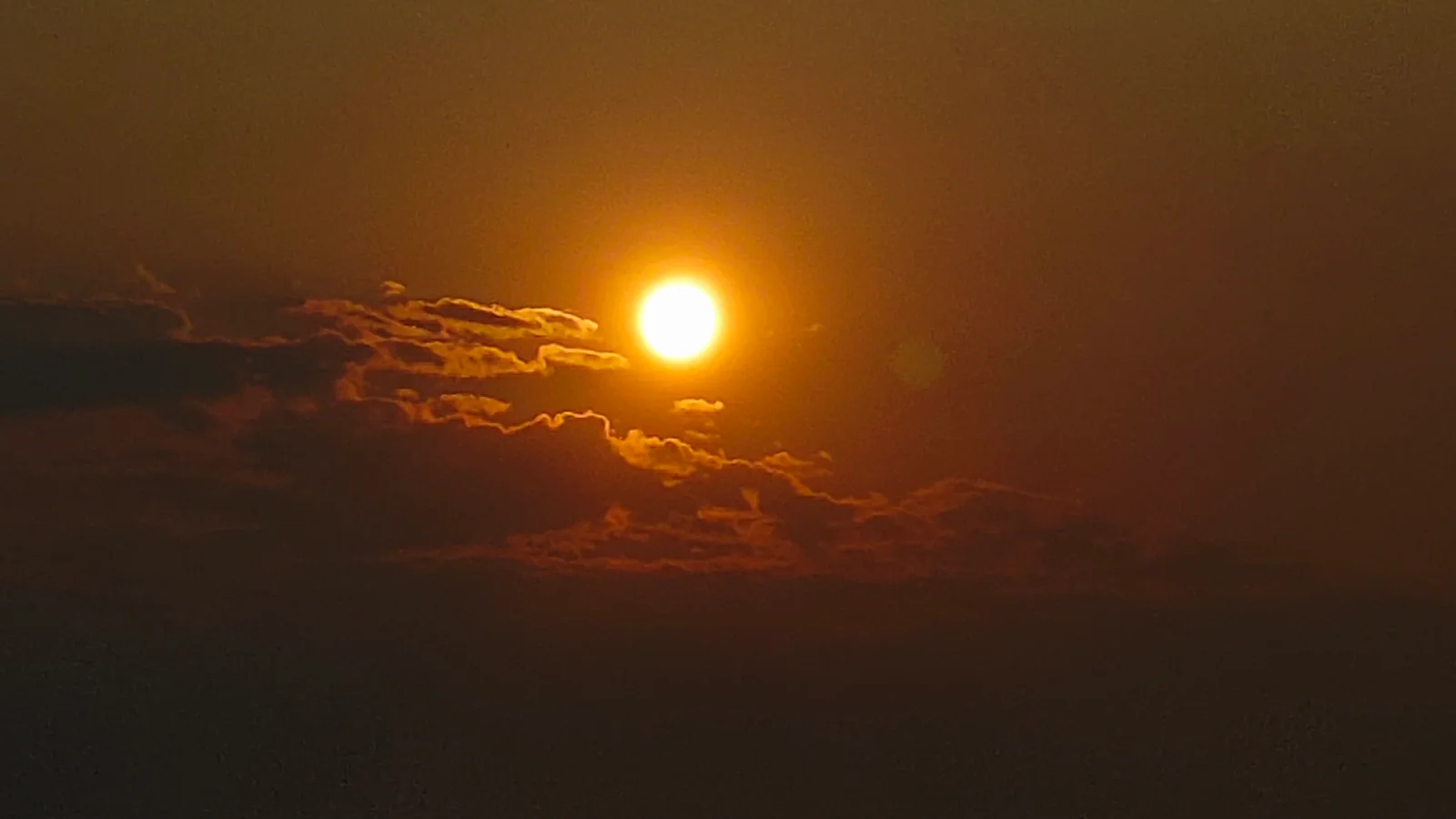 The bright sun sits above a dark cloud bank at dusk.