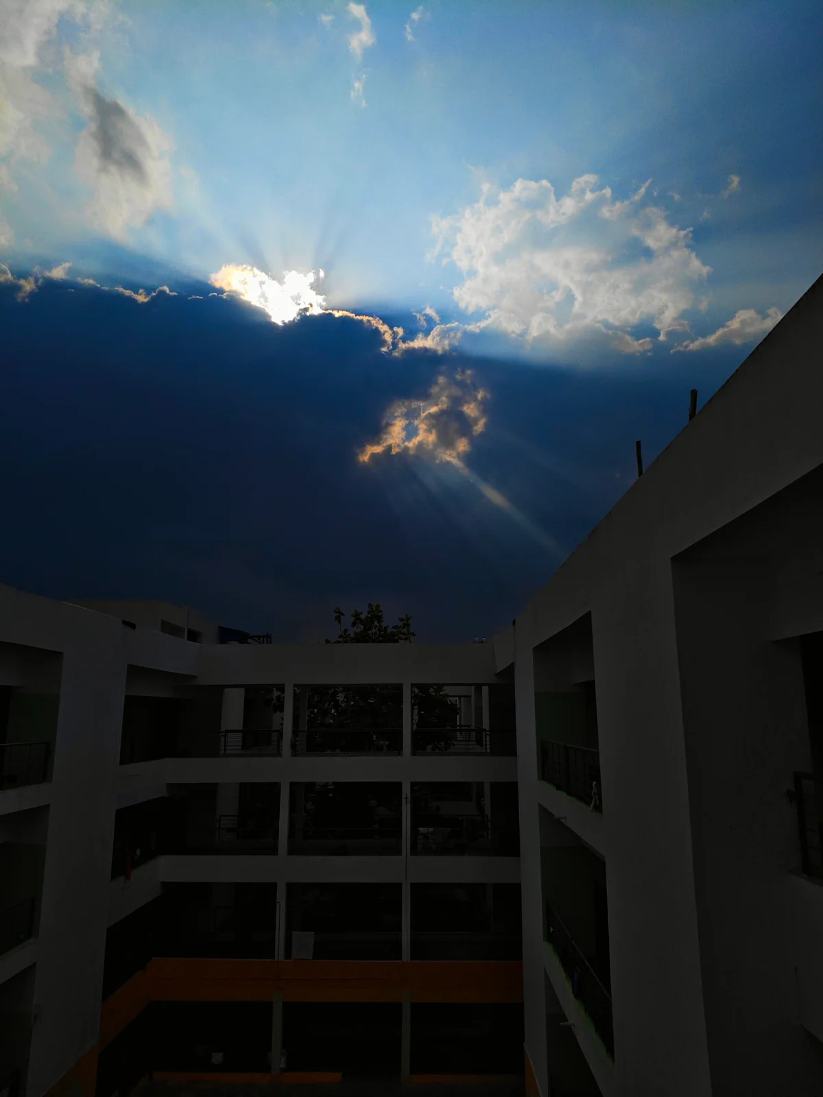 Sunlight breaks through clouds above a dark building courtyard.